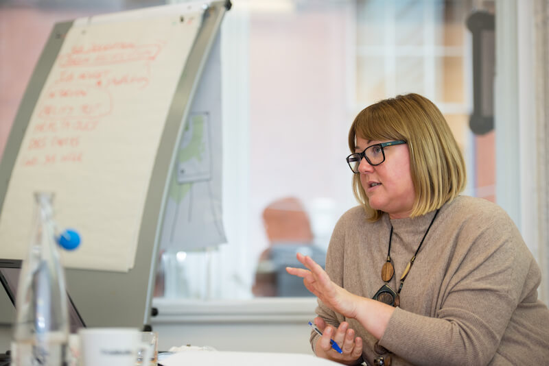 Alison sits at a table, talking to other people within a HR training session